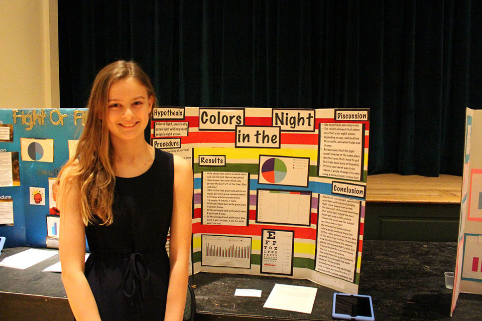 ACDS science female student smiling in front of science project